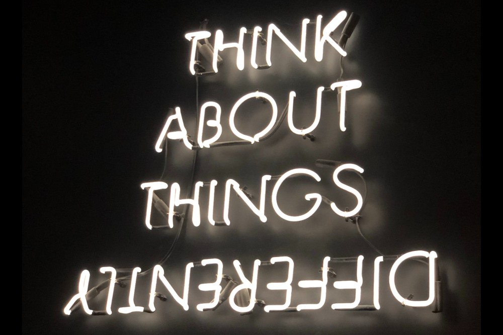 Neon sign saying "think about things differently" regarding the ideal worker.