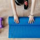 Woman rolling up yoga mat with dumbells next to it in her home gym setup.