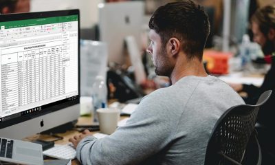 Spreadsheets open on desktop with man in office setting.