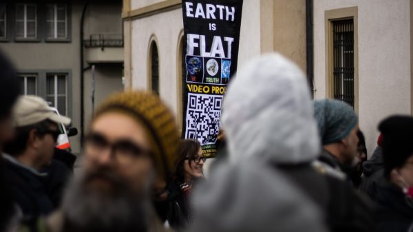 earth is flat sign in the middle of a crowd representing attach of personal beliefs