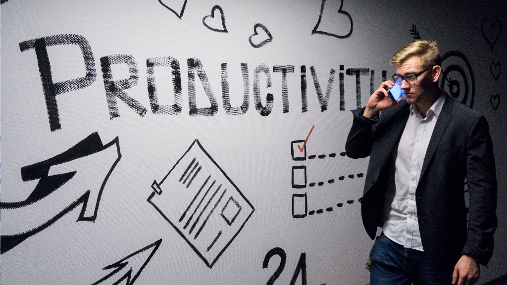 productivity written on wall with man on cellphone.