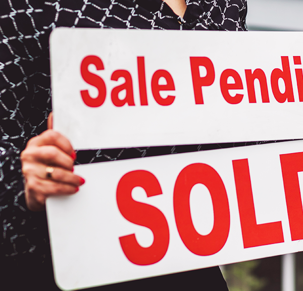 A person with painted red nails holding a 'sale pending' and a 'sold' sign in a home selling marketplace.