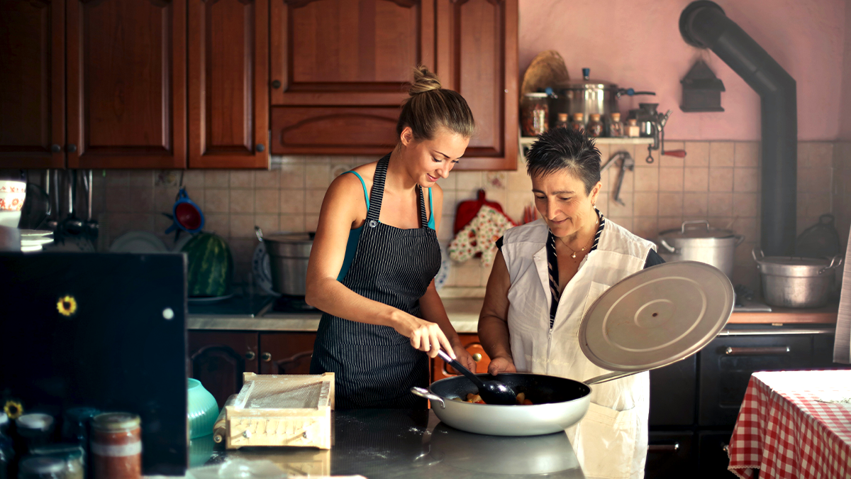 A mother and daughter cook together in a warmly decorated kitchen, part of a trend of multi-generational housing.