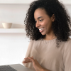 A Black woman holds a laptop in a white office space, smiling as she clicks on the keyboard leaving reviews