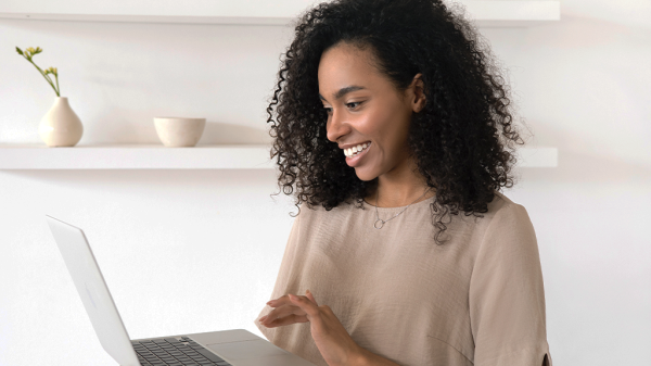 A Black woman holds a laptop in a white office space, smiling as she clicks on the keyboard leaving reviews
