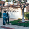 A young couple holding each other as they stand outside of a house pondering homeownership.