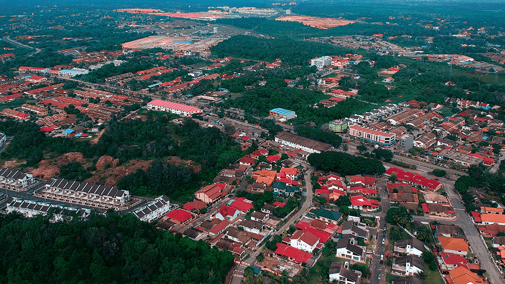 An aerial view of a suburban neighborhood with many occupied and vacant homes with red rooves surrounded by green trees.
