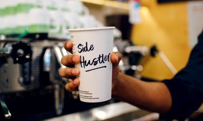 Coffee cup with side hustle written on it representing overemployment.