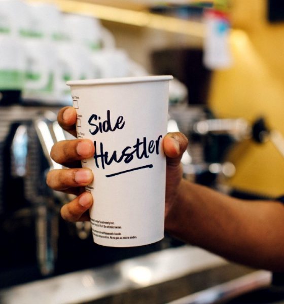 Coffee cup with side hustle written on it representing overemployment.
