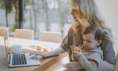 A woman holding a baby on her lap doing remote work.
