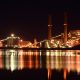 Manufacturing plant at night across the water with orange and red reflections.