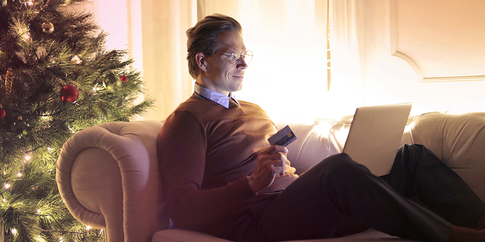 Man on laptop open to Twitter, considering his holiday shopping with Christmas tree behind him.