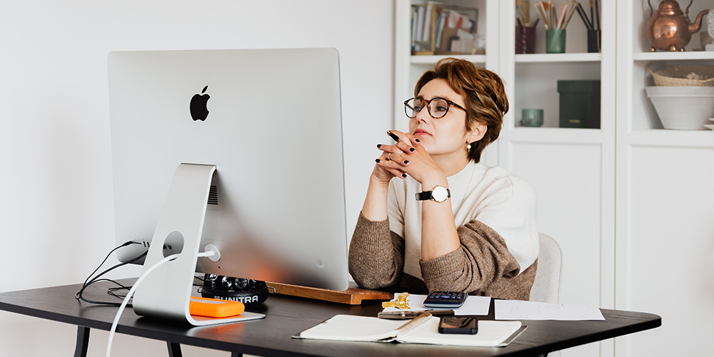Woman sitting at computer with fingers steepled, awaiting a rejection email or any response from HR at all.