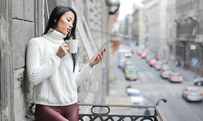 Woman checking social media on her phone on a balcony overlooking city traffic.