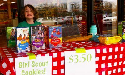 Girl Scouts table selling cookies with smiling young girl behind the table.