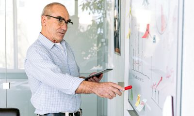 Balding man in glasses at a whiteboard, using supplies from Office Depot.