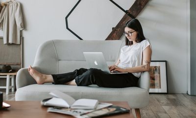 Woman working remotely on her couch with a laptop on her lap.