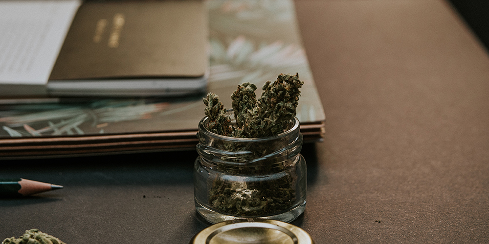 A small jar of cannabis on a desk with notebooks, sold online in a nicely made jar.