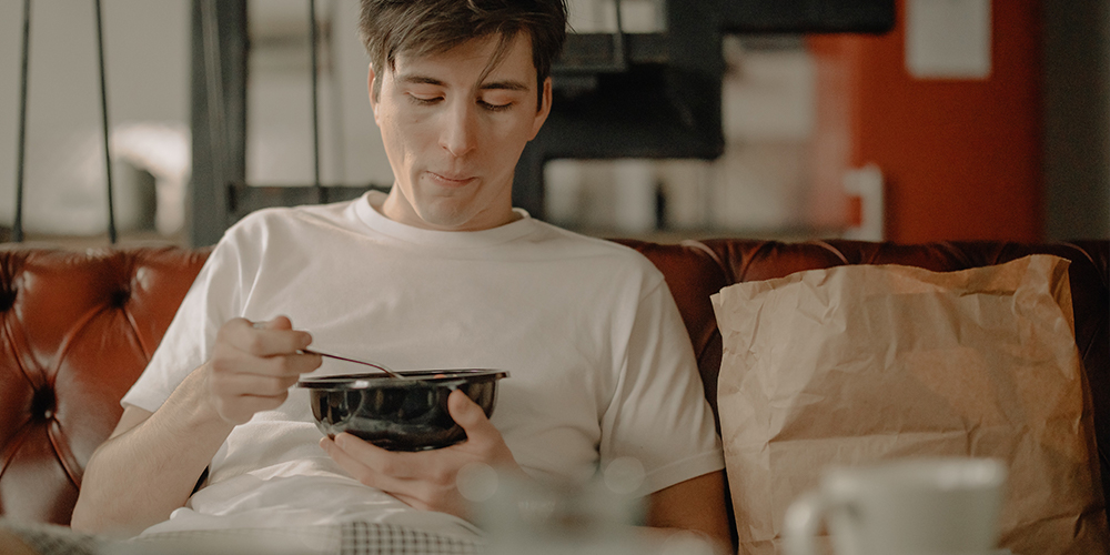 Man seated on couch eating food from a food delivery person.