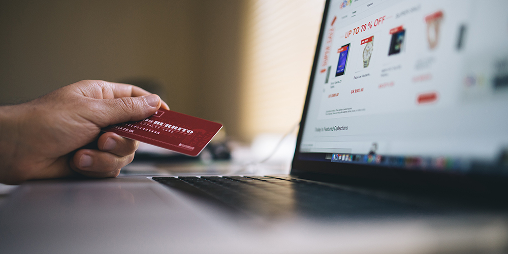 Ecommerce site open on a laptop with a hand holding a credit card next to the screen for shopping.