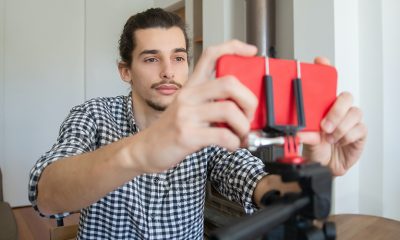 Man in front a red smartphone on a stand, setting up for a live stream.