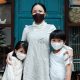 Woman in front of small business with two children, all wearing face masks