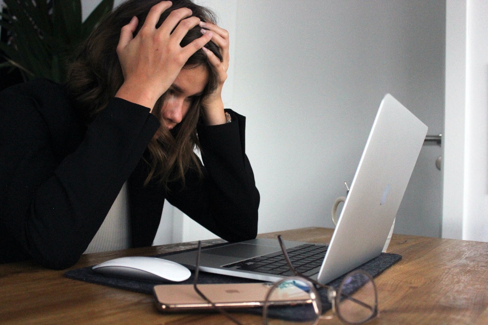 Woman holding head in hands in front of laptop frustrated with job seeking.