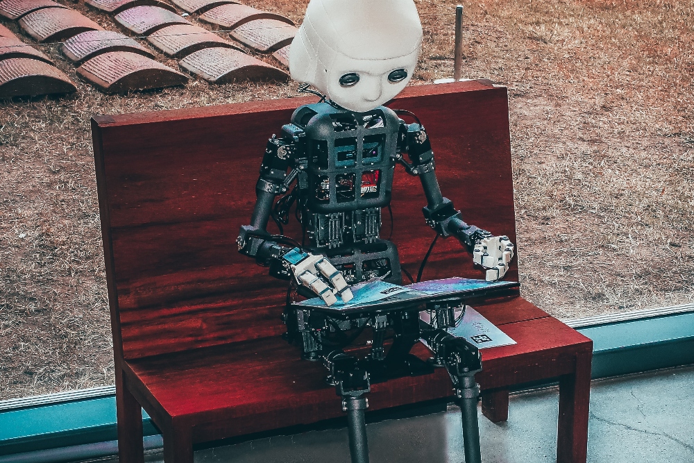 Robot sitting on bench with large iPad representing AI