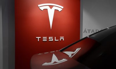 Tesla showroom with red wall panel and T logo reflecting off the trunk of a Tesla car.