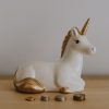 Unicorn piggy bank on desk with coins in front.