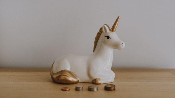 Unicorn piggy bank on desk with coins in front.