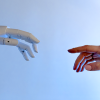 A human hand reaches out to a robot hand against a pale blue and white background. AI ethics have regularly come into play, and now more than ever.