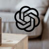A wooden-cased Alexa sits on a coffee table in a living room, positioned next to a logo of ChatGPT