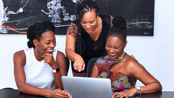 Three Black women are looking at a computer and chatting excitedly. Layoffs have led to a lot of innovation and new LLCs being formed.
