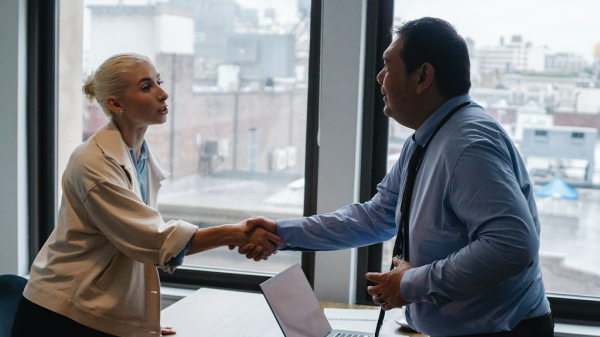 A woman and man shake hands in a friendly manner in a business office. With the labor shortage, new hires are always welcome.