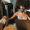 A woman sitting in a warm morning room sipping coffee and petting a soft brown dog while she looks at her computer for job salary listings.