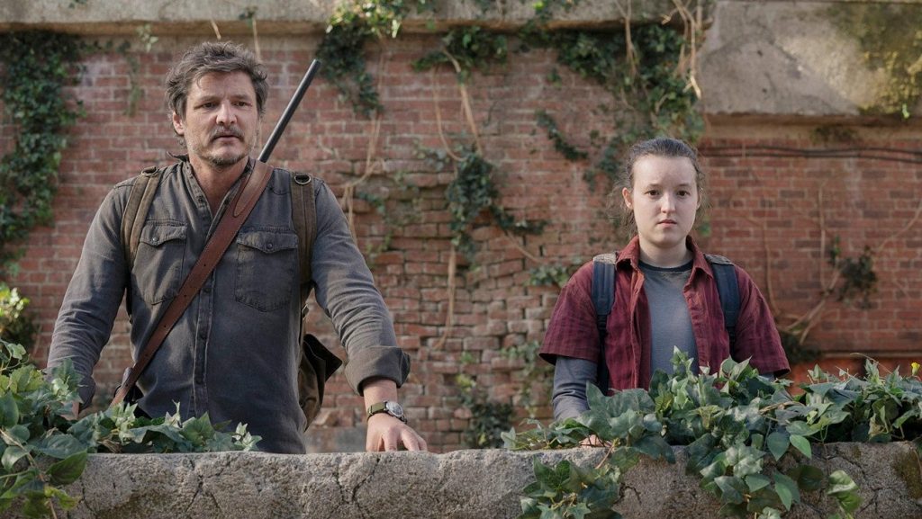 A scene from The Last of Us featuring Joel (Pedro Pascal) and Ellie (Bella Ramsey) looking out over an ivy-grown wall.
