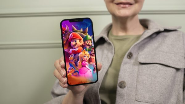 A woman holding up a phone with the Super Mario Brothers movie poster displayed on its screen, inspired by the video game.