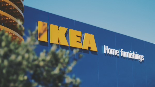 A storefront of IKEA, with a blue wall and yellow text, and a small bush in front of the storefront.
