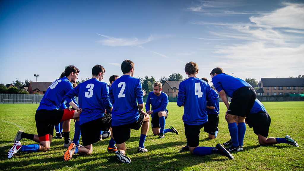 A group of men kneeling in blue soccer jerseys playing in sports and fitness with a variety of equipment around them and a neighborhood in the background.