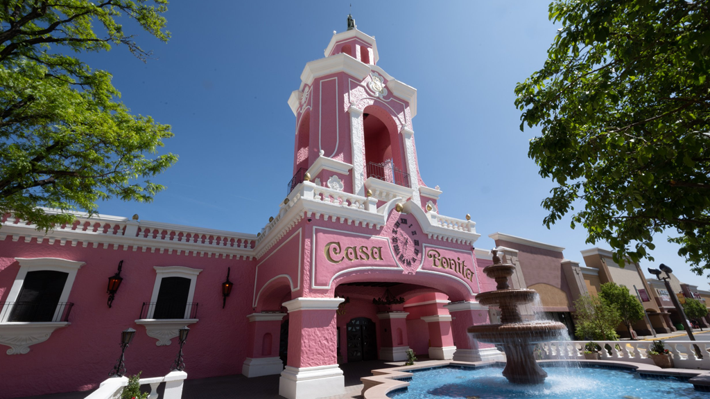 The front of Casa Bonita, a large ornate pink building with a tall tower in the center and white steeples.