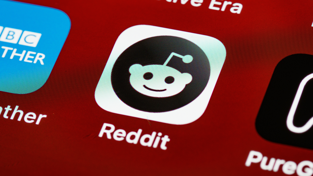 An darkened app icon for Reddit on a red screen surrounded by a other mobile app icons.