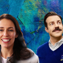 A picture of character Ted Lasso and former New Zealand Prime Minister Jacinda Ardern standing together on a blue painted background, two figures in leadership.