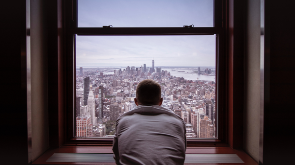 A man leans against a broad windowsill overlooking a city, being thoughtful about change.