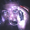 A bearded man holding up fairy lights up to his face to illuminate his face in a blue-purple light representing neurotechnology.