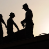 Silhouettes of three men working on a rooftop in the labor market.