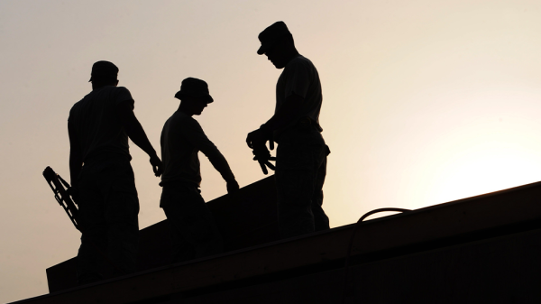 Silhouettes of three men working on a rooftop in the labor market.
