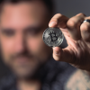 A man holding up a crypto bitcoin to the camera with the camera focused on the coin in his hand.