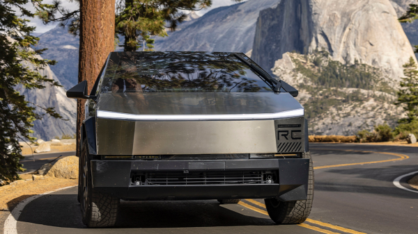 A Tesla cybertruck driving along a mountain forest road with a large mountain in the background.