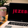 A laptop computer on a desk with a coffee and smart phone next to it. The logo for Jezebel, the news site, is pulled up on the screen.